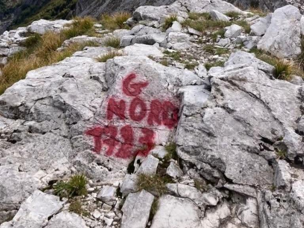 Escursionista imbratta con una bomboletta spray di vernice rossa alcune rocce sulle Alpi Apuane
