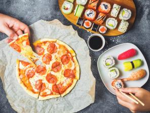 Tasty Pizza with salami, set of sushi rolls and hands take food. Dark background. Flat lay, top view.