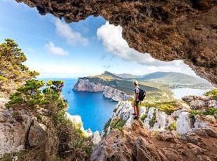 Capo Caccia, hiker admiring the view from a cave. Sardinia island, Ital