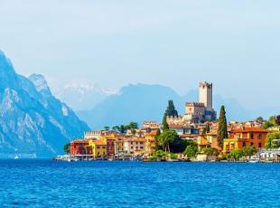 Ancient tower and fortress in old town malcesine at garda lake veneto region italy high snowbound top mountains on background summer landscape with colorful houses green tree