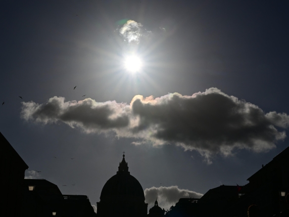 This photograph taken from Rome shows the sun shining over a cloud and the dome of St Peter's Basilica of the Vatican, a day prior to the Pope's funeral, on April 25, 2025. The Vatican on April 25, 2025, said 150,000 people have already paid their respects to Pope Francis, whose body is lying in state in St Peter's Basilica ahead of his funeral. (Photo by Andrej ISAKOVIC / AFP)