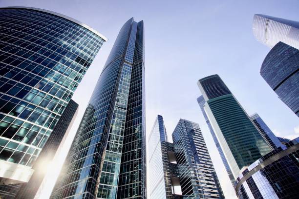 Office and residential skyscrapers against bright sun and clear blue sky. Commercial real estate. Glass and metal in urban architecture. High-tech facade design. Modern business city district. Office buildings exterior. Financial city district. Reflections and highlights in glass. Wide angle city photography
