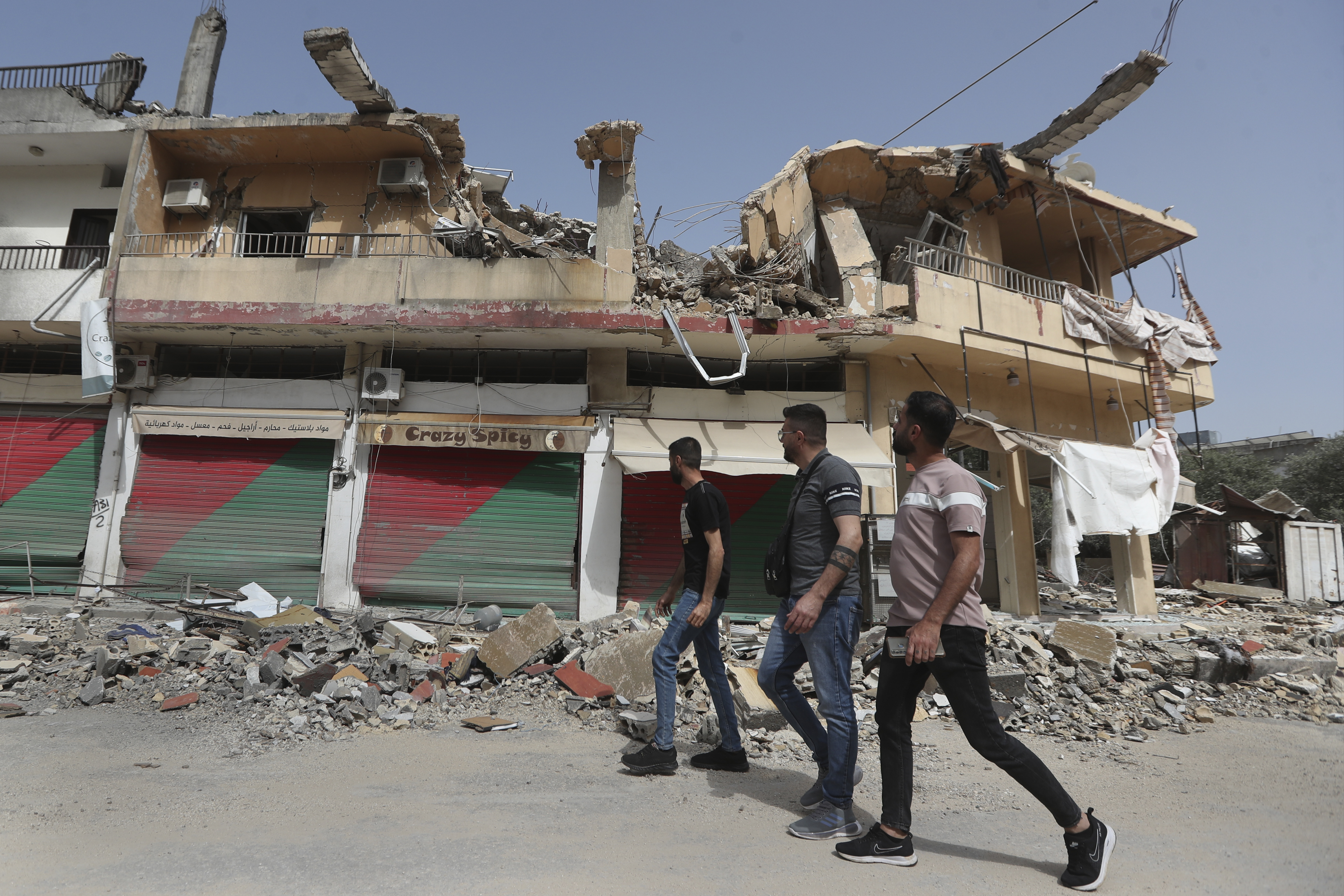 Lebanese villagers pass by a building which was destroyed by Israeli shelling, in Kfar Kila, a Lebanese border village with Israel, south Lebanon, Thursday, April 18, 2024. Hezbollah militants and Israeli forces have been exchanging fire since a day after the Israel-Hamas war began on Oct. 7. (AP Photo/Mohammed Zaatari)