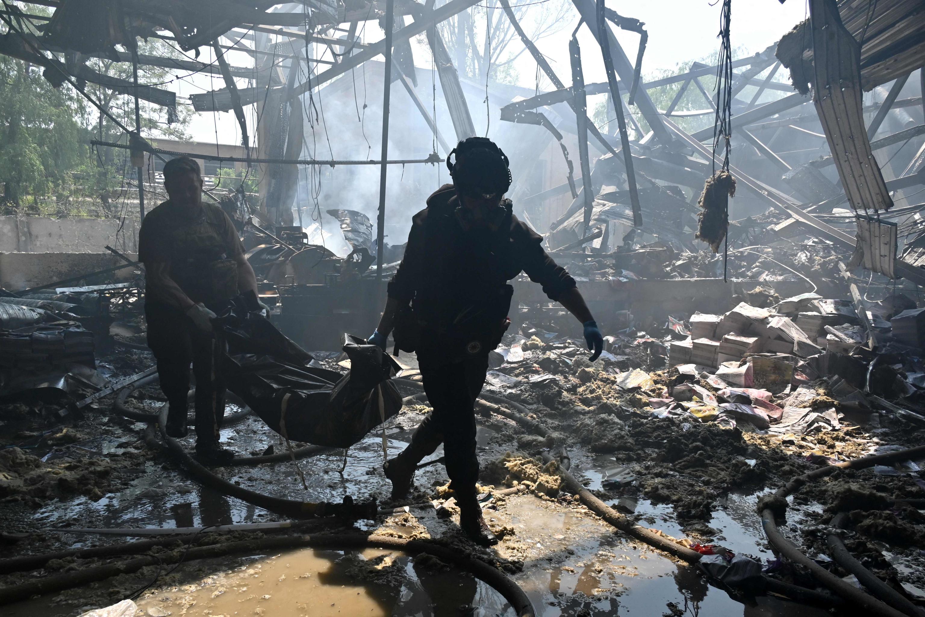 EDITORS NOTE: Graphic content / TOPSHOT - Law enforcement officers carry the body of a person, killed during a missile attack in Kharkiv on May 23, 2024, amid the Russian invasion of Ukraine. Russian strikes on Ukraine's second-largest city Kharkiv killed at least seven people, authorities said on May 23, 2024, as Moscow claimed fresh advances on the front line. (Photo by SERGEY BOBOK / AFP)