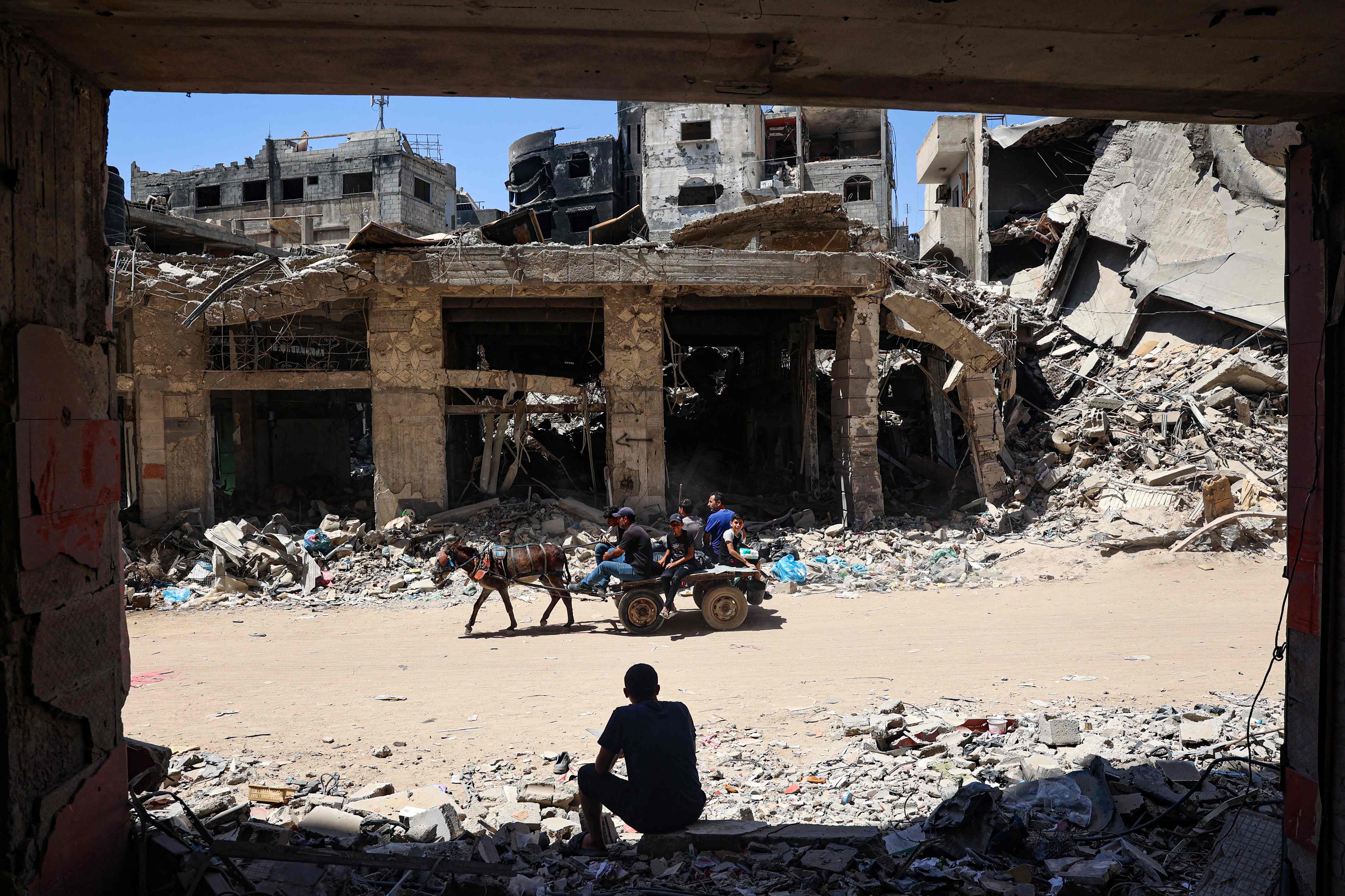 TOPSHOT - A man looks on as displaced Palestinians ride a donkey-pulled cart along a devastated street in Khan Yunis in the southern Gaza Strip on May 24, 2024, amid the ongoing conflict between Israel and Hamas. (Photo by Eyad BABA / AFP)