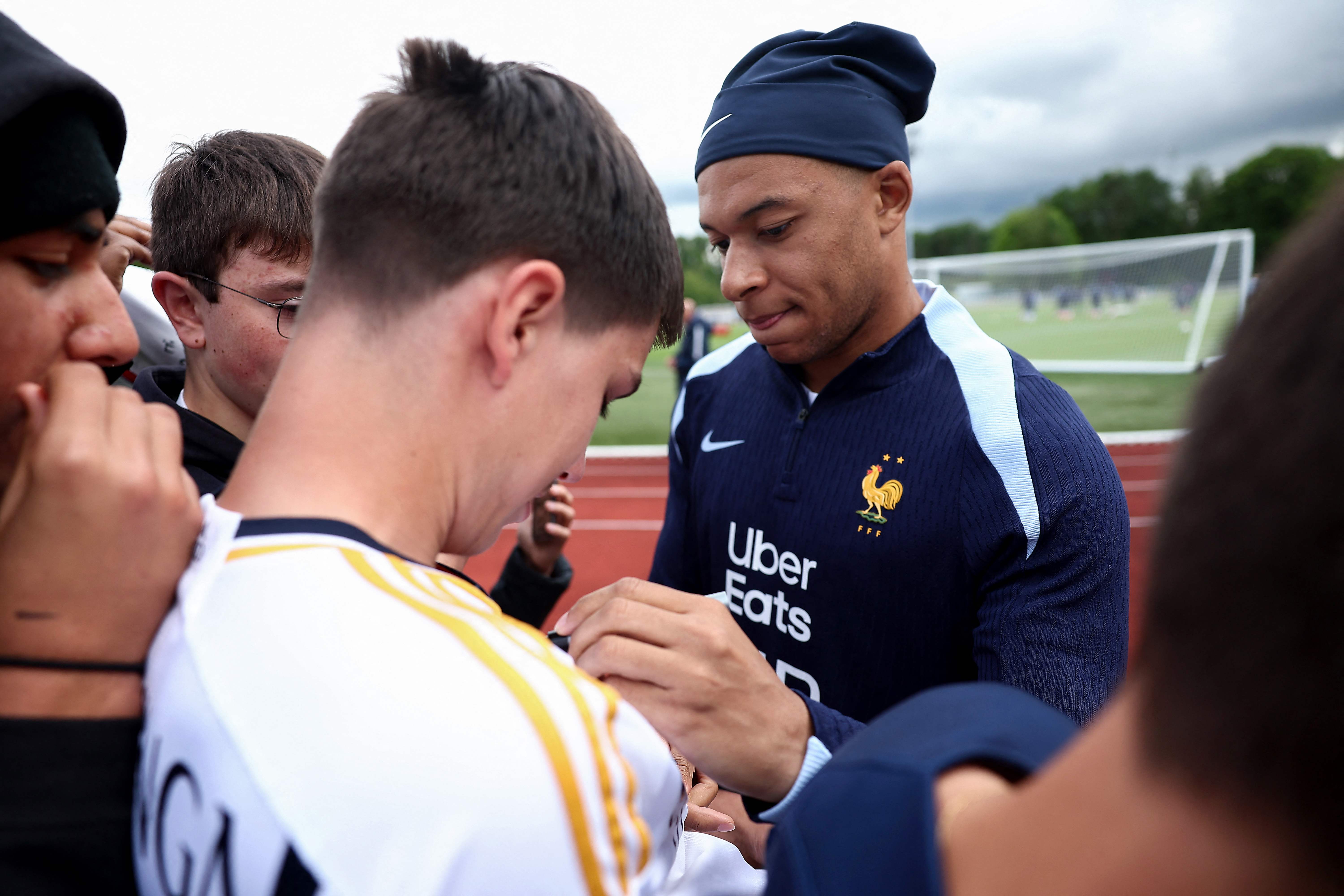 France's forward Kylian Mbappe (R) signs an autograph for a fan wearing a Real Madrid jersey, ahead of a training session, as part of the team's preparation for upcoming UEFA Euro 2024 Football Championship, in Clairefontaine-en-Yvelines on May 30, 2024. Having been crowned European champions for the 15th time, Real Madrid have completed another successful season, but the festivities are likely to continue for a long time to come, with the imminent transfer of Kylian MbappE expected to be made official early next week. (Photo by FRANCK FIFE / AFP)