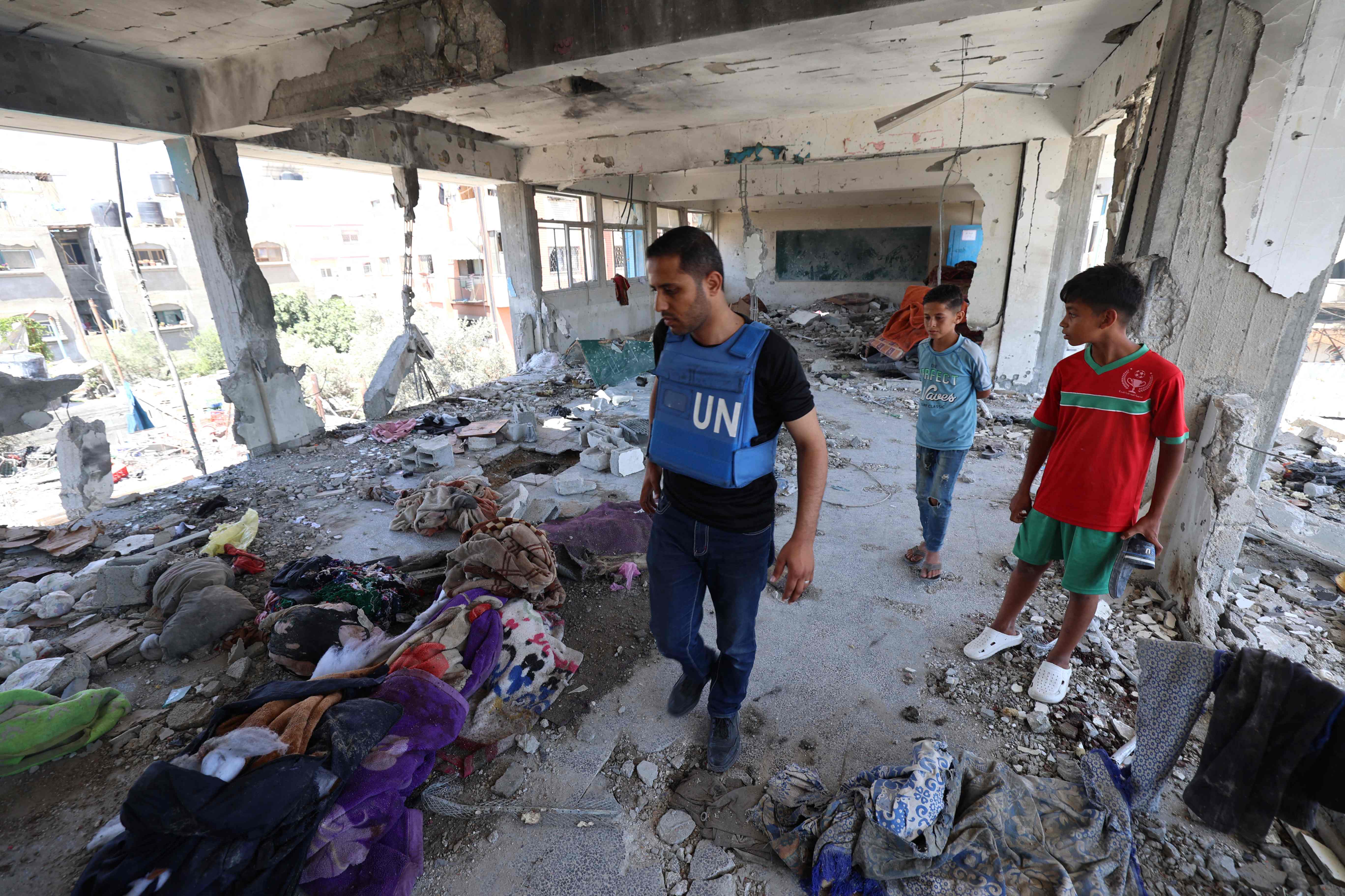 Palestinian boys watch as a member of a United Nations investigation team as he visits a school run by the UN Relief and Works Agency for Palestine Refugees (UNRWA) which was hit during an Israeli army strike the day before, in the Nuseirat camp in the central Gaza Strip on June 7, 2024, amid the ongoing conflict in the Palestinian territory between Israel and Hamas. The United Nations agency for Palestinian refugees, UNRWA, said hundreds of displaced Gazans were sheltering at the school, which was "hit without prior warning" on June 6. (Photo by Eyad BABA / AFP)