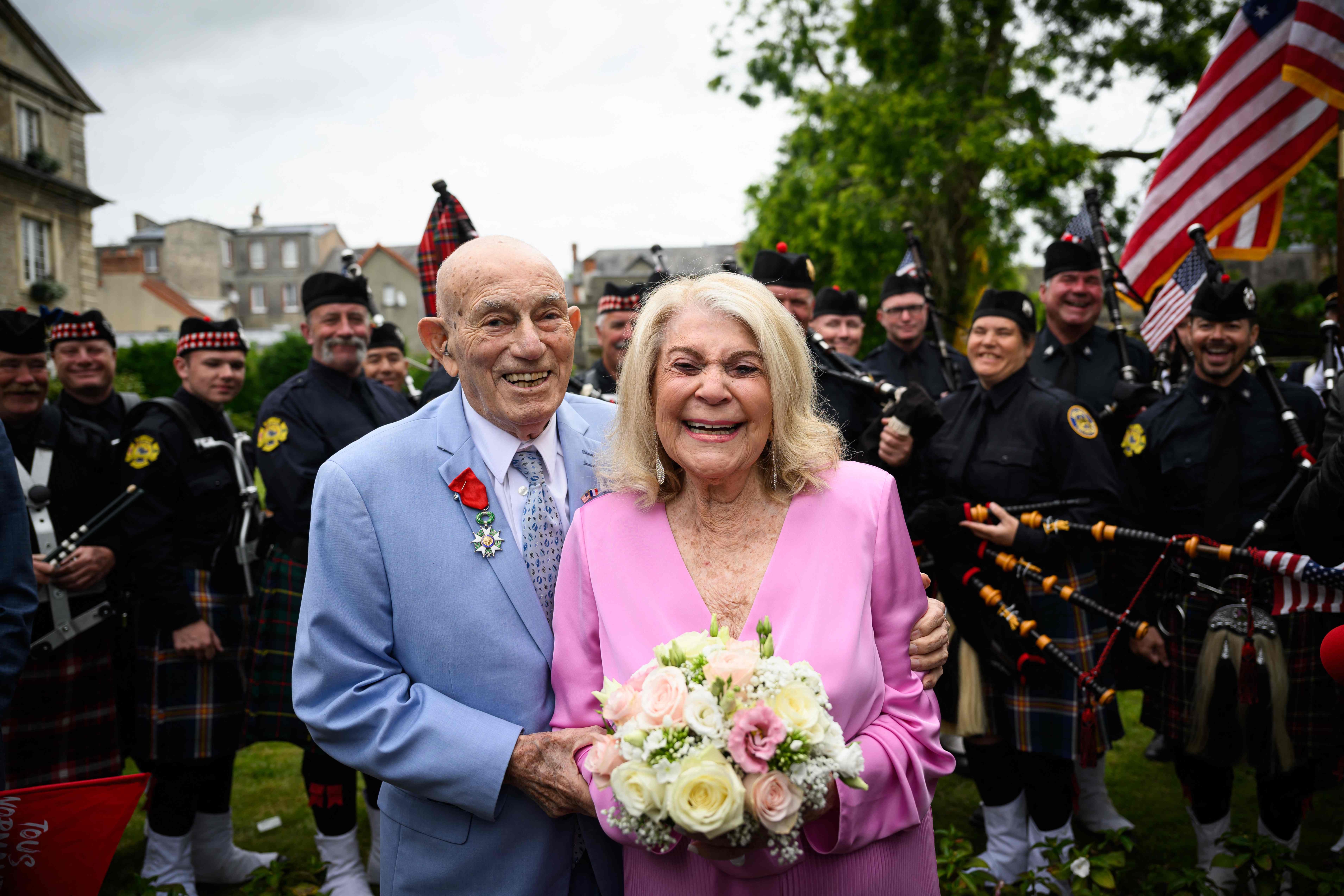 Newly-weds Jeanne Swerlin, 96, (R) and US WWII veteran Harold Terens, 100, (L) pose for photographs in front of a piper band as they celebrate their marriage during a wedding at the town hall of Carentan-les-Marais, in Normandy, northwestern France, on June 8, 2024, just days after being honoured on the 80th anniversary of the D-Day landings that took place a few kilometres away. The D-Day ceremonies on June 6 this year marked the 80th anniversary since the launch of 'Operation Overlord', a vast military operation by Allied forces in Normandy, which turned the tide of World War II, eventually leading to the liberation of occupied France and the end of the war against Nazi Germany. (Photo by LOIC VENANCE / AFP)