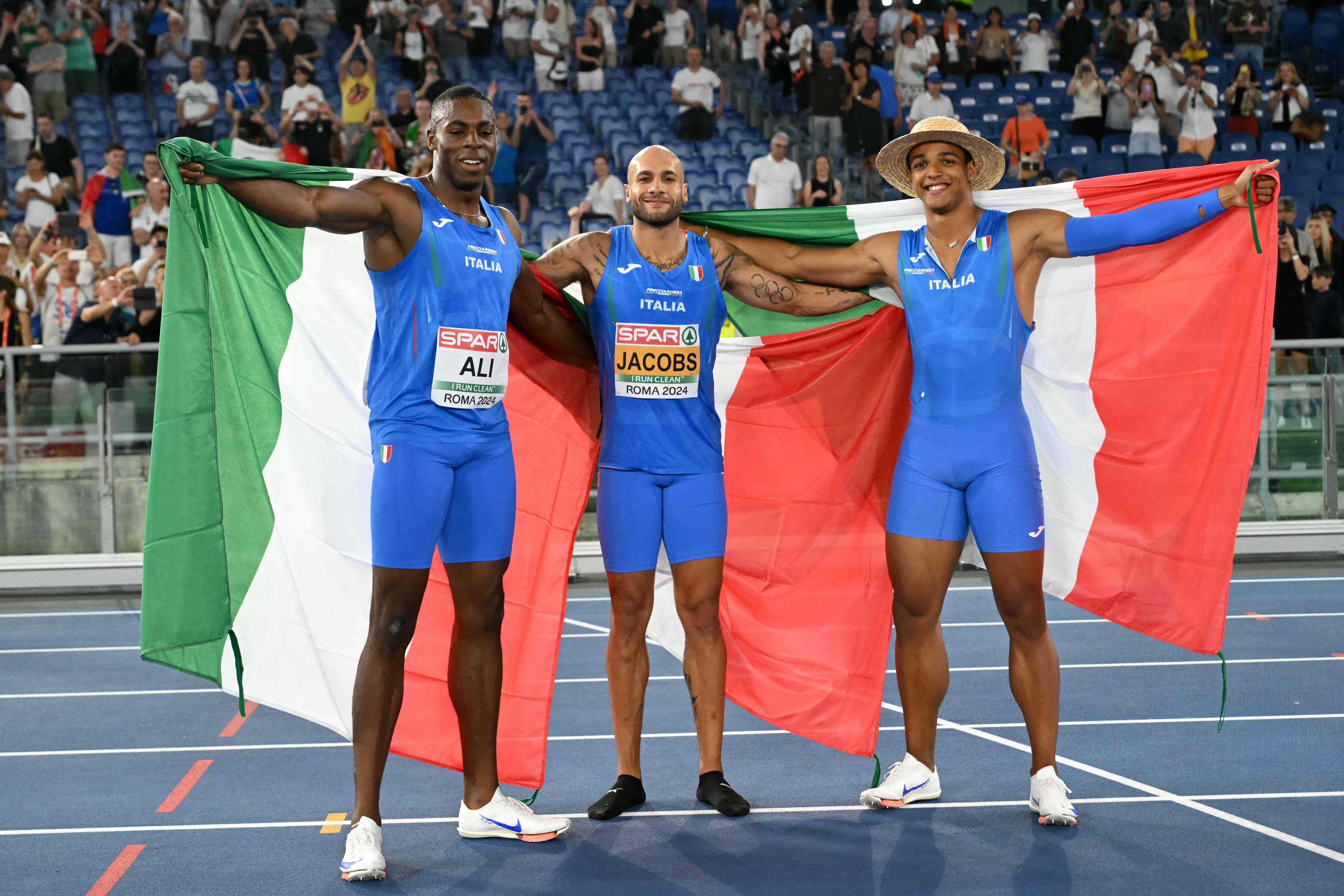 100m silver medallist Italy's athlete Chituru Ali, 100m gold medallist Italy's Lamont Marcell Jacobs and 110m hurdles gold medallist Italy's Lorenzo Ndele Simonelli pose with flags during the European Athletics Championships at the Olympic stadium in Rome on June 8, 2024. (Photo by Andreas SOLARO / AFP)