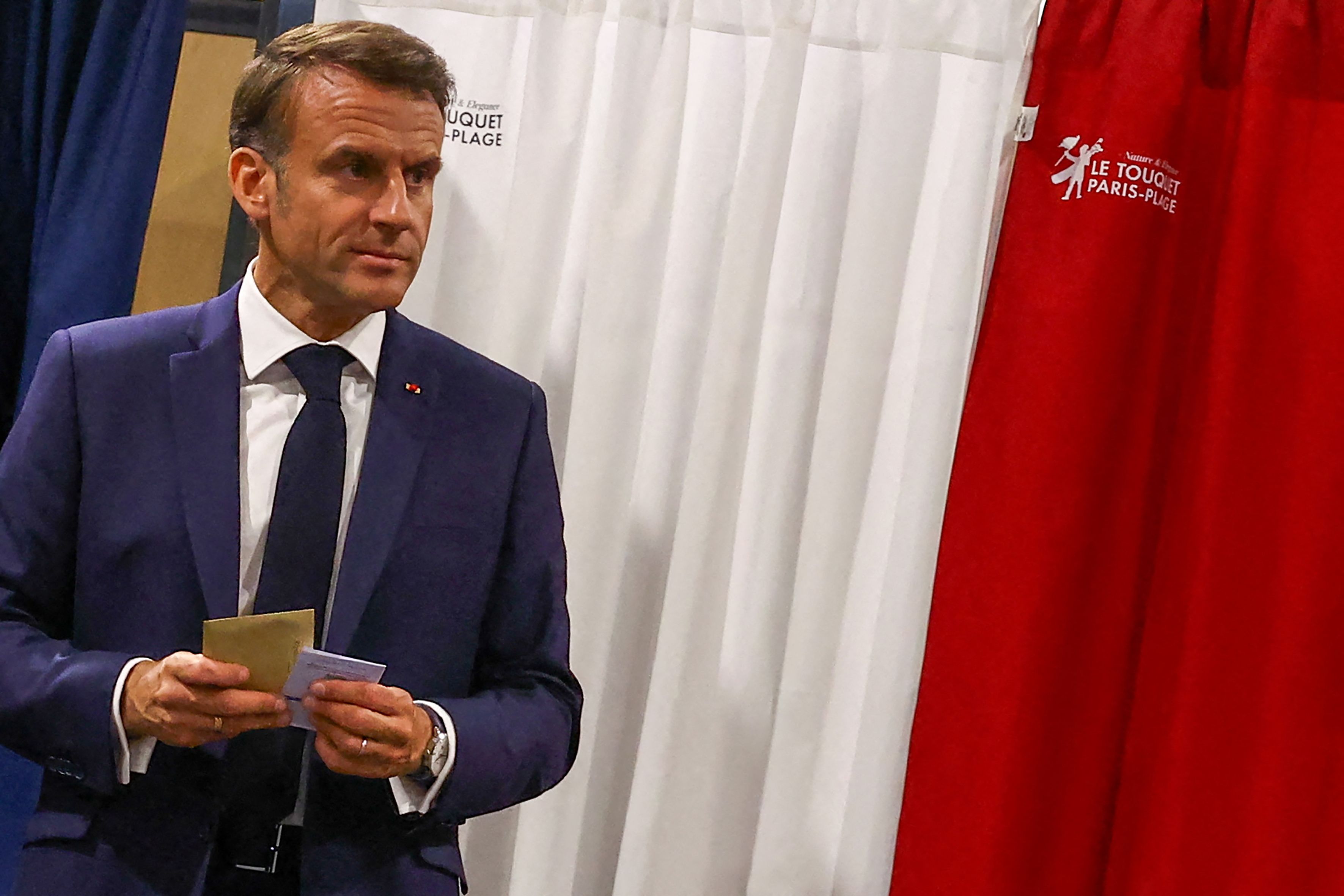 France's President Emmanuel Macron exits a polling booth, adorned with curtains displaying the colors of the flag of France, before casting his ballot for the European Parliament election at a polling station in Le Touquet, northern France on June 9, 2024. Voting began across Europe on June 9, 2024 on the final -- and biggest -- day of marathon EU elections, with balloting due in 21 countries, including France and Germany, where support for surging far-right parties is being tested. (Photo by Hannah McKay / POOL / AFP)