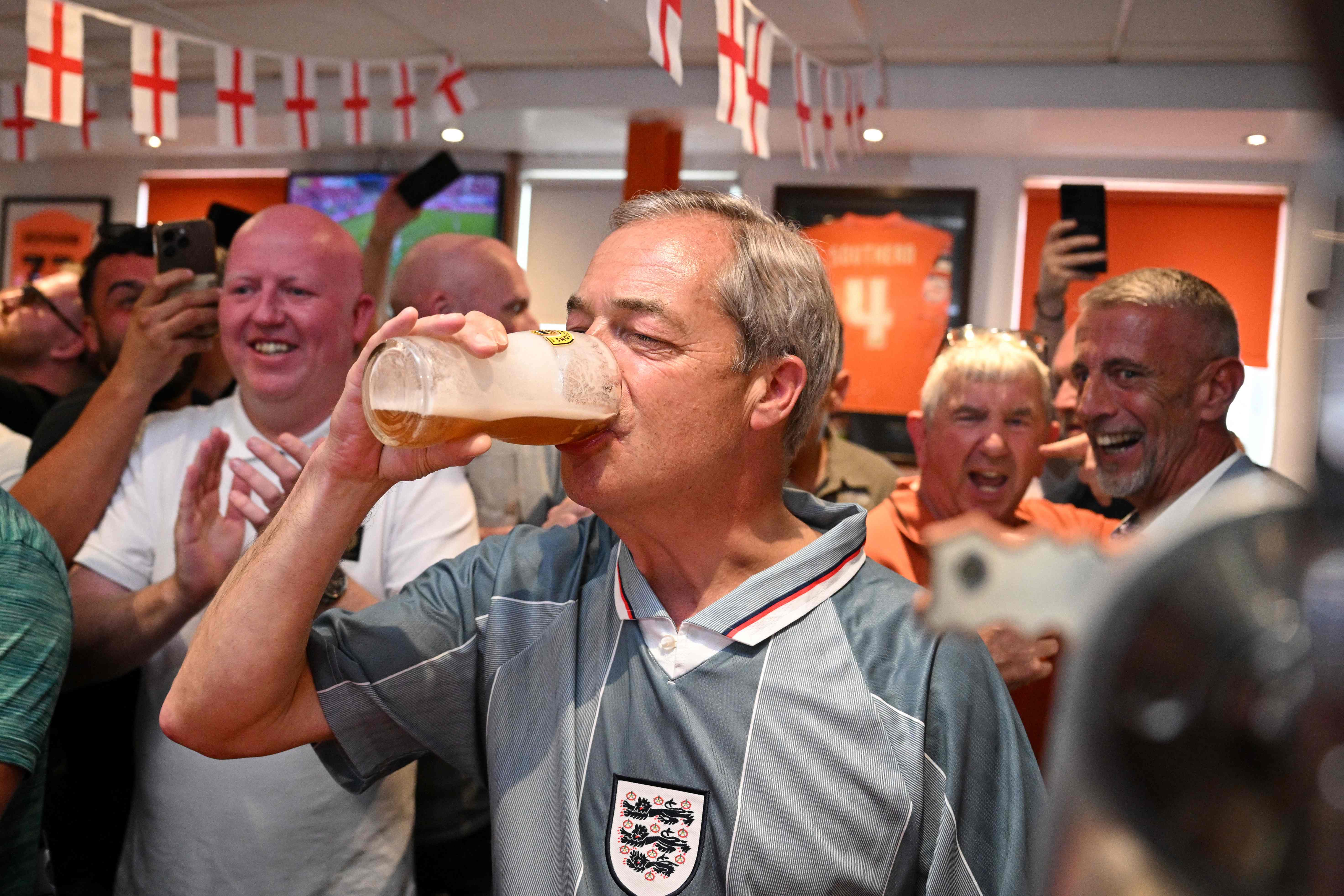 Leader of Reform UK Nigel Farage wearing a 1996 England football shirt drinks beer as he joins England football fans watching a live broadcast of the UEFA Euro 2024 Group C football match between Denmark and England at The Armfield Club in Blackpool, northwestern England, on June 20, 2024, in the build-up to the UK general election on July 4. (Photo by Oli SCARFF / AFP)