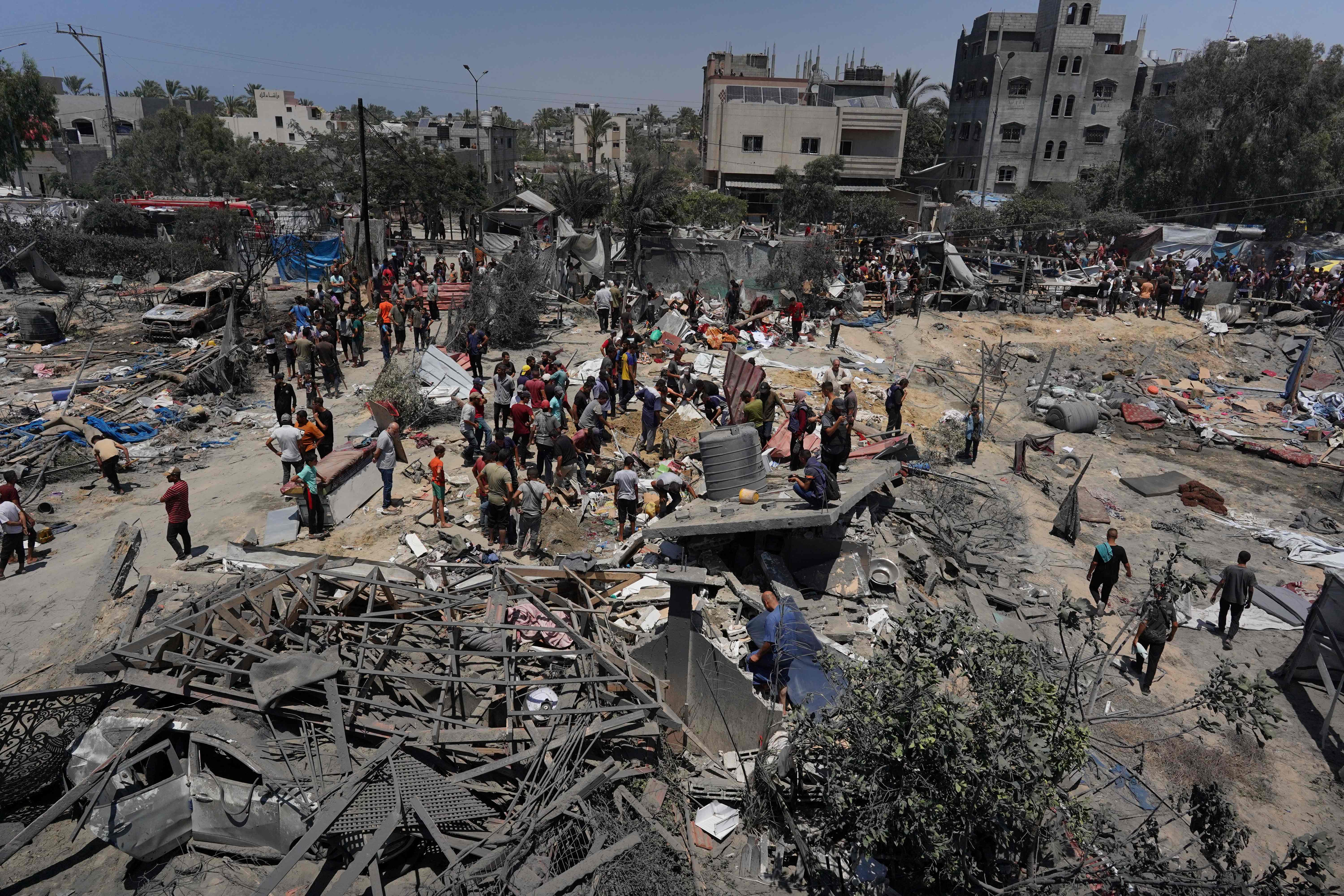 TOPSHOT - Palestinians look at the debris of destroyed tents and make shift housing structures following an Israeli military strike on the al-Mawasi camp for internally displaced people (IDP), near the city of Khan Yunis, southern Gaza Strip on July 13, 2024, in which killing 71 people were killed. Al-Mawasi had been declared a safe zone by Israel as it pursues its military offensive in other parts of the Gaza Strip in response to the October 7 Hamas attacks. (Photo by Bashar TALEB / AFP)