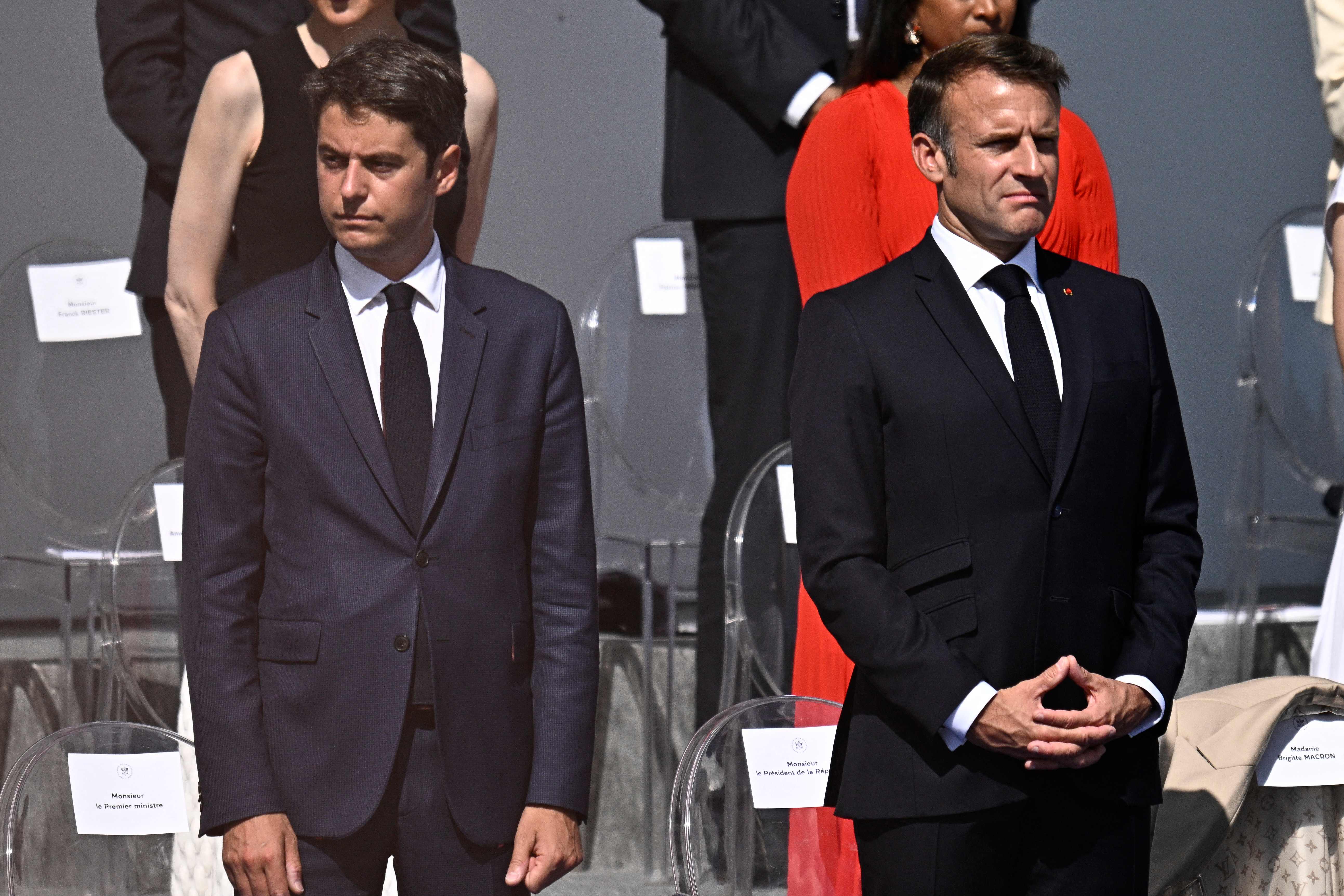 TOPSHOT - France's Prime Minister Gabriel Attal (L) reacts next to France's President Emmanuel Macron during the Bastille Day military parade on the Avenue Foch in Paris on July 14, 2024. (Photo by JULIEN DE ROSA / AFP)