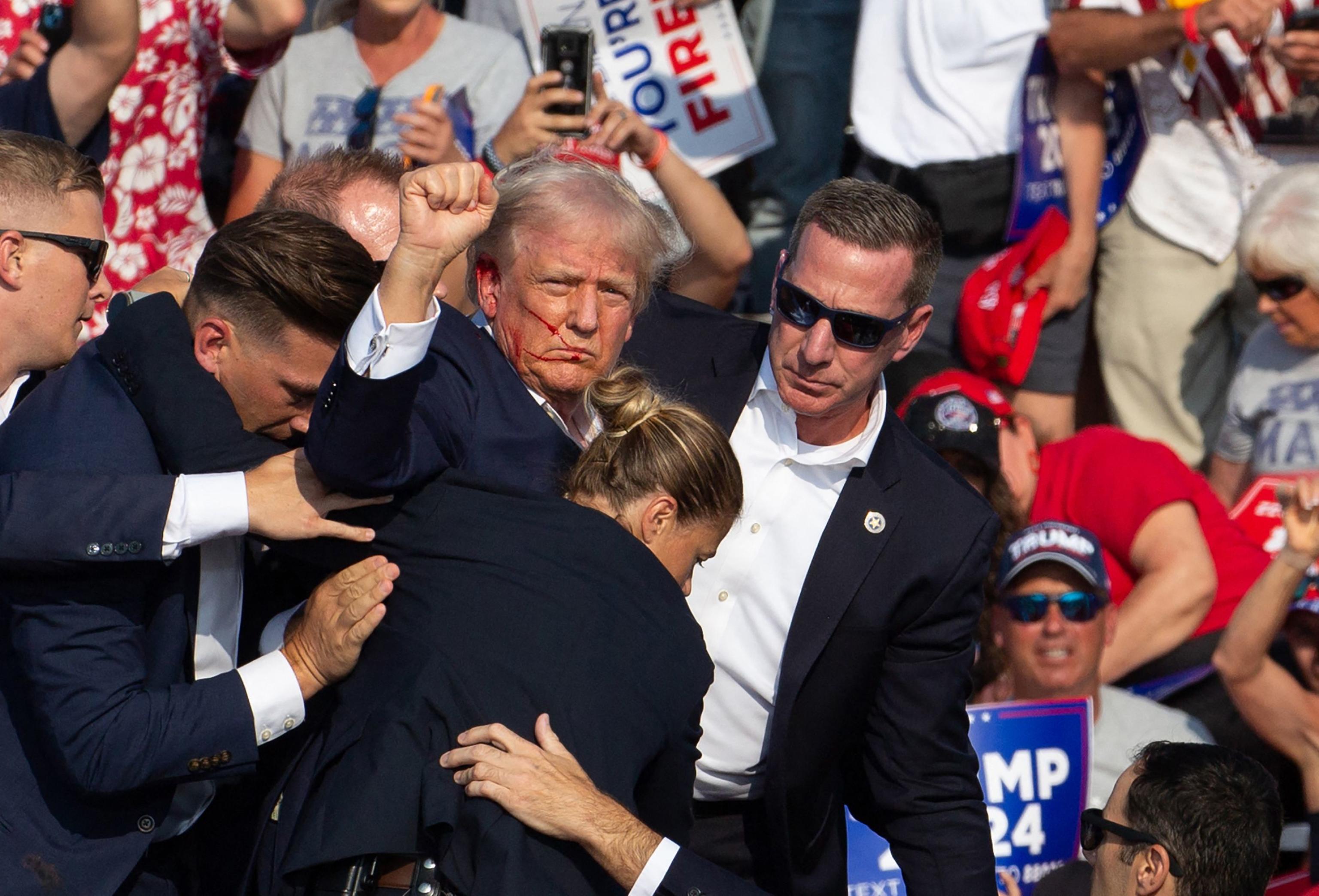 Republican candidate Donald Trump is seen with blood on his face surrounded by secret service agents as he is taken off the stage at a campaign event at Butler Farm Show Inc. in Butler, Pennsylvania, July 13, 2024. Donald Trump was hit in the ear in an apparent assassination attempt by a gunman at a campaign rally on Saturday, in a chaotic and shocking incident that will fuel fears of instability ahead of the 2024 US presidential election. The 78-year-old former president was rushed off stage with blood smeared across his face after the shooting in Butler, Pennsylvania, while the gunman and a bystander were killed and two spectators critically injured. (Photo by Rebecca DROKE / AFP)