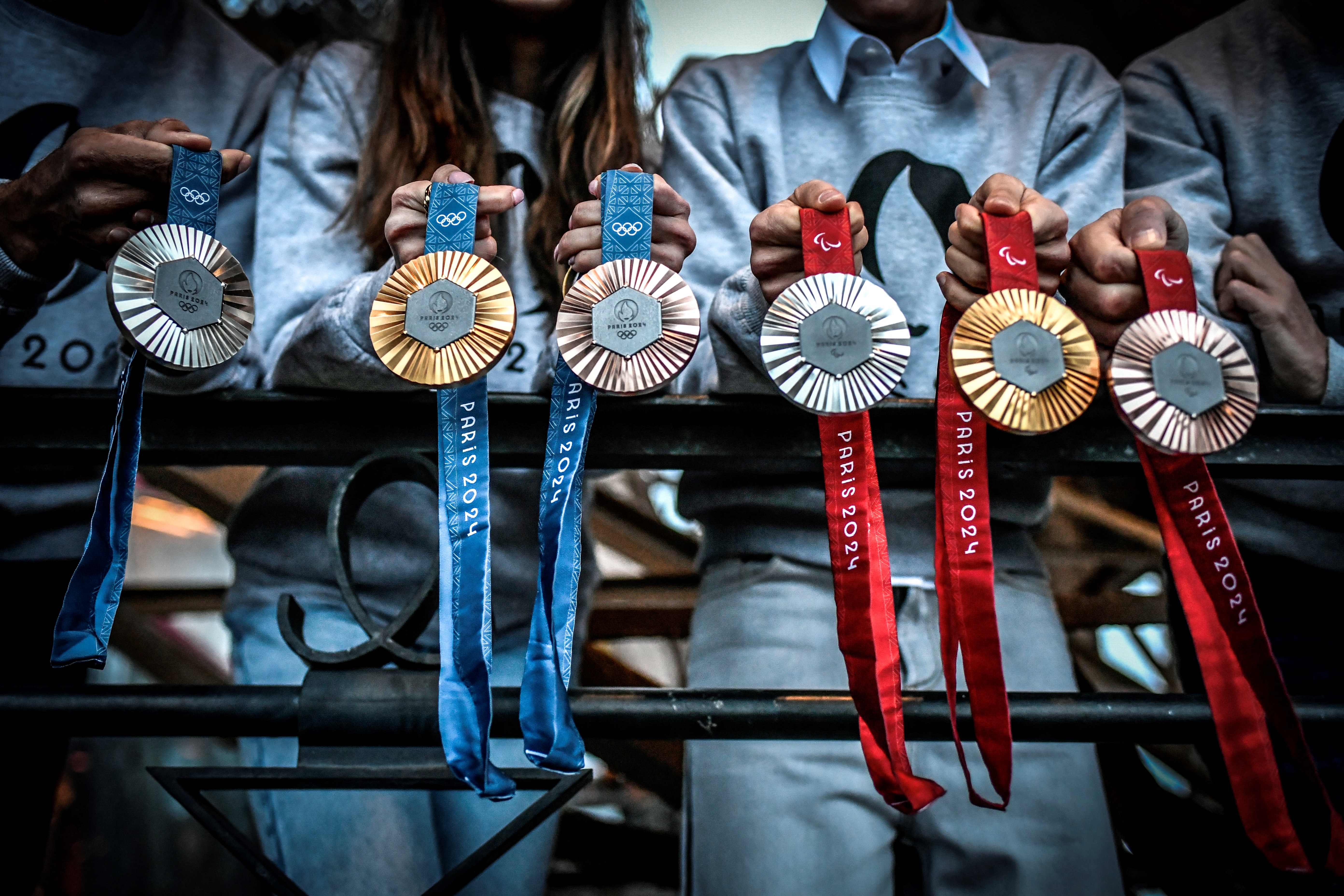 This picture shows upcoming Paris 2024 Olympics medals designed by Fench luxury jewellery house Chaumet, on February 01, 2024 during their presentation at the Eiffel tower in Paris. On the medals' head side, the engraved figures of the goddess of victory Athena, Nike, the Panathenaic stadium and the Acropolis are imposed by the International Olympic Committee (IOC) but Paris 2024 has obtained exceptional authorization to add the design of the Eiffel Tower, and use 18 grams of Eiffel Tower metal on each medal, extracted from pieces of the tower. (Photo by STEPHANE DE SAKUTIN / AFP)
