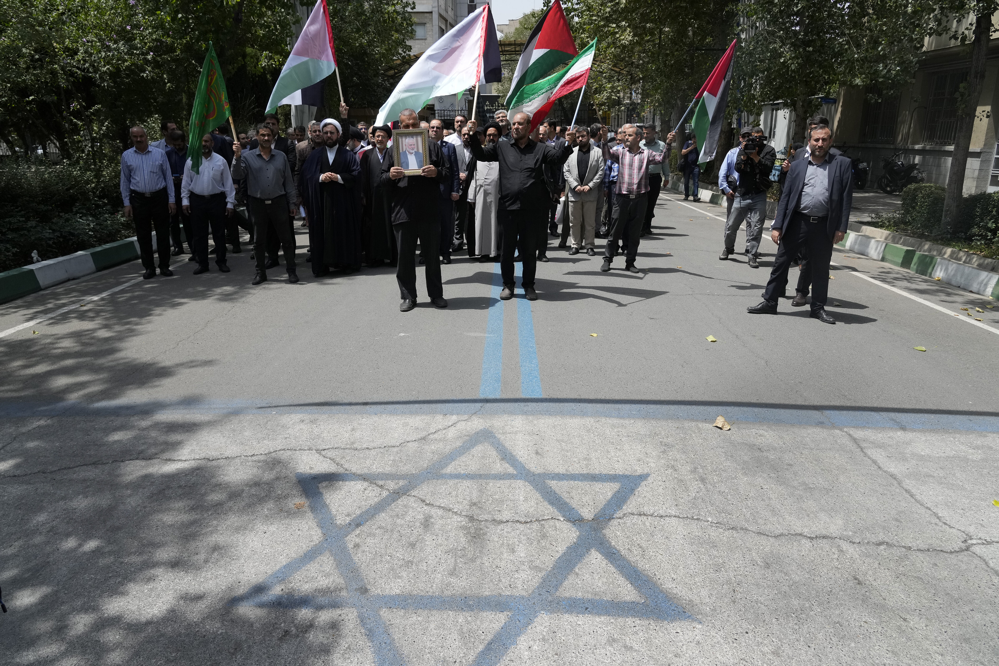 Members of Tehran University Council attend a protest to condemn the killing of Hamas political chief Ismail Haniyeh as they carry Iranian and Palestinian flags, while an image of the Israeli flag is painted on the ground at the University, in Tehran, Iran, Wednesday, July 31, 2024. Haniyeh, Hamas' political chief in exile, was killed in an airstrike in the Iranian capital early Wednesday. (AP Photo/Vahid Salemi)