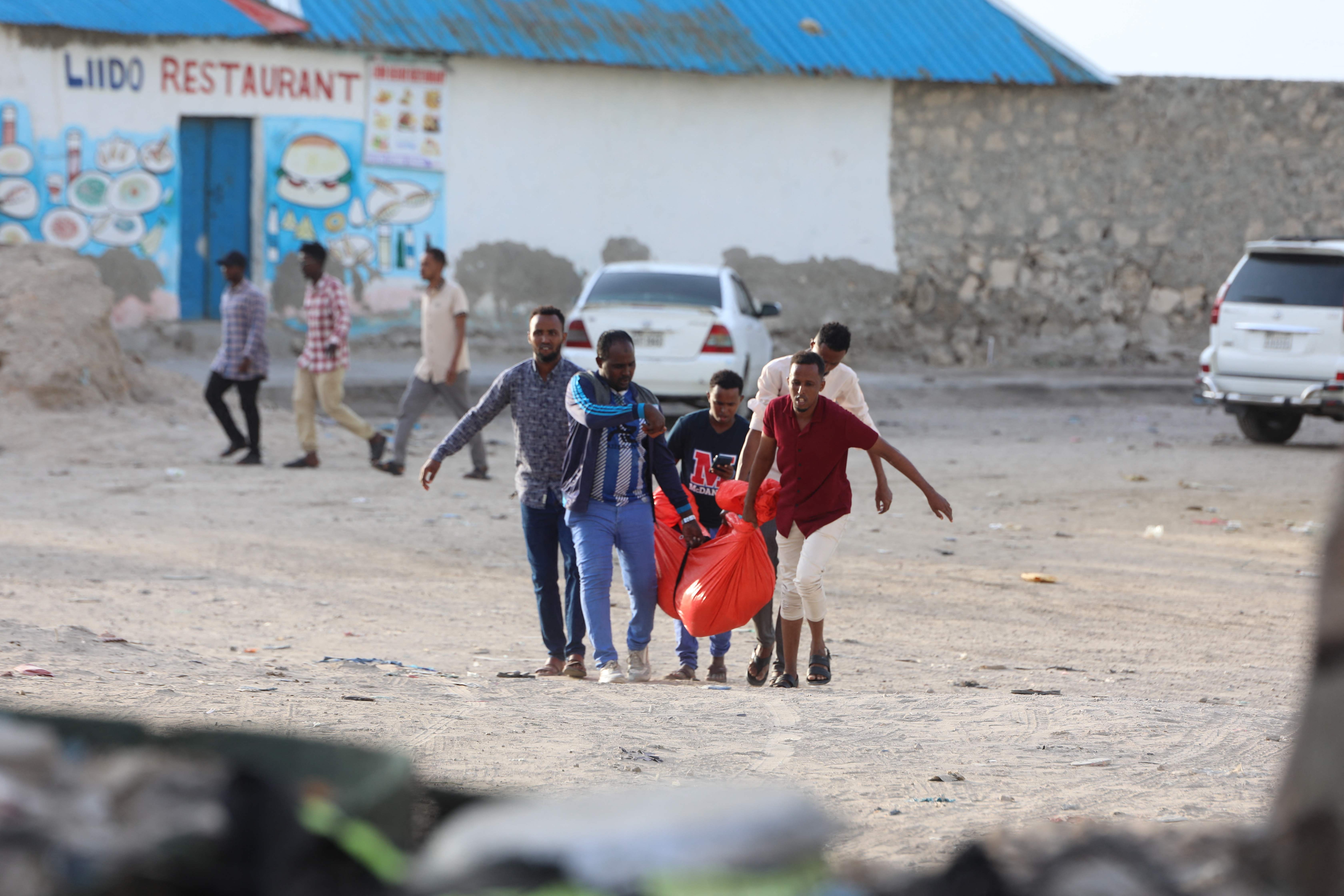 Relatives carry the body of a woman killed during an attack in Mogadishu on August 3, 2024. An Al-Shabaab suicide bomber and gunmen attacked a busy beachfront spot in the Somali capital Mogadishu killing at least seven people, police said Saturday. Police and witnesses told AFP the bomber detonated his device late Friday along Lido Beach -- popular with business people and officials and the scene of previous attacks -- before gunmen stormed the area. (Photo by Hassan Ali ELMI / AFP)