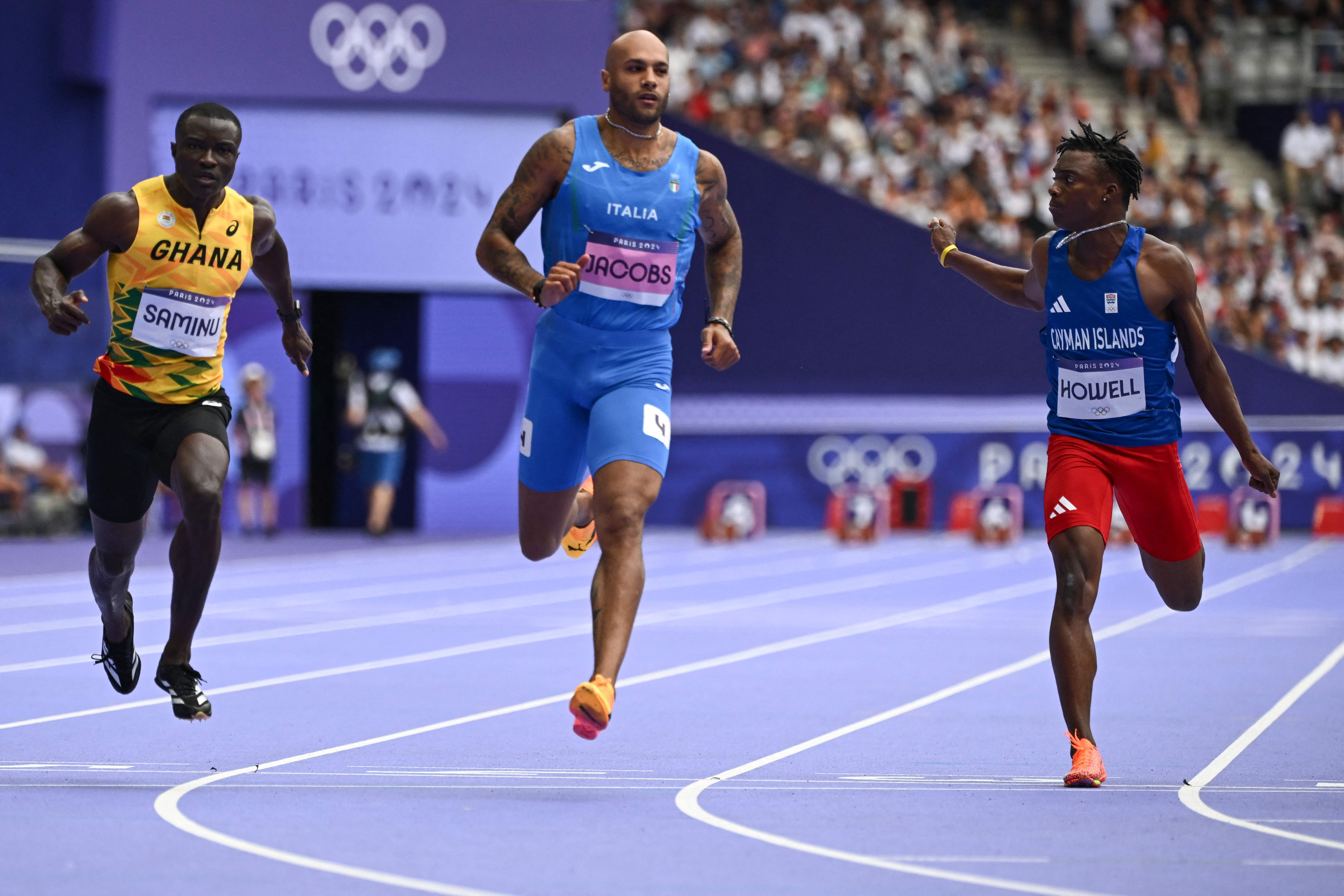 (From L) Ghana's Abdul-Rasheed Saminu, Italy's Lamont Marcell Jacobs and Cayman Islands' Davonte Howell compete in the men's 100m heat of the athletics event at the Paris 2024 Olympic Games at Stade de France in Saint-Denis, north of Paris, on August 3, 2024. (Photo by Jewel SAMAD / AFP)