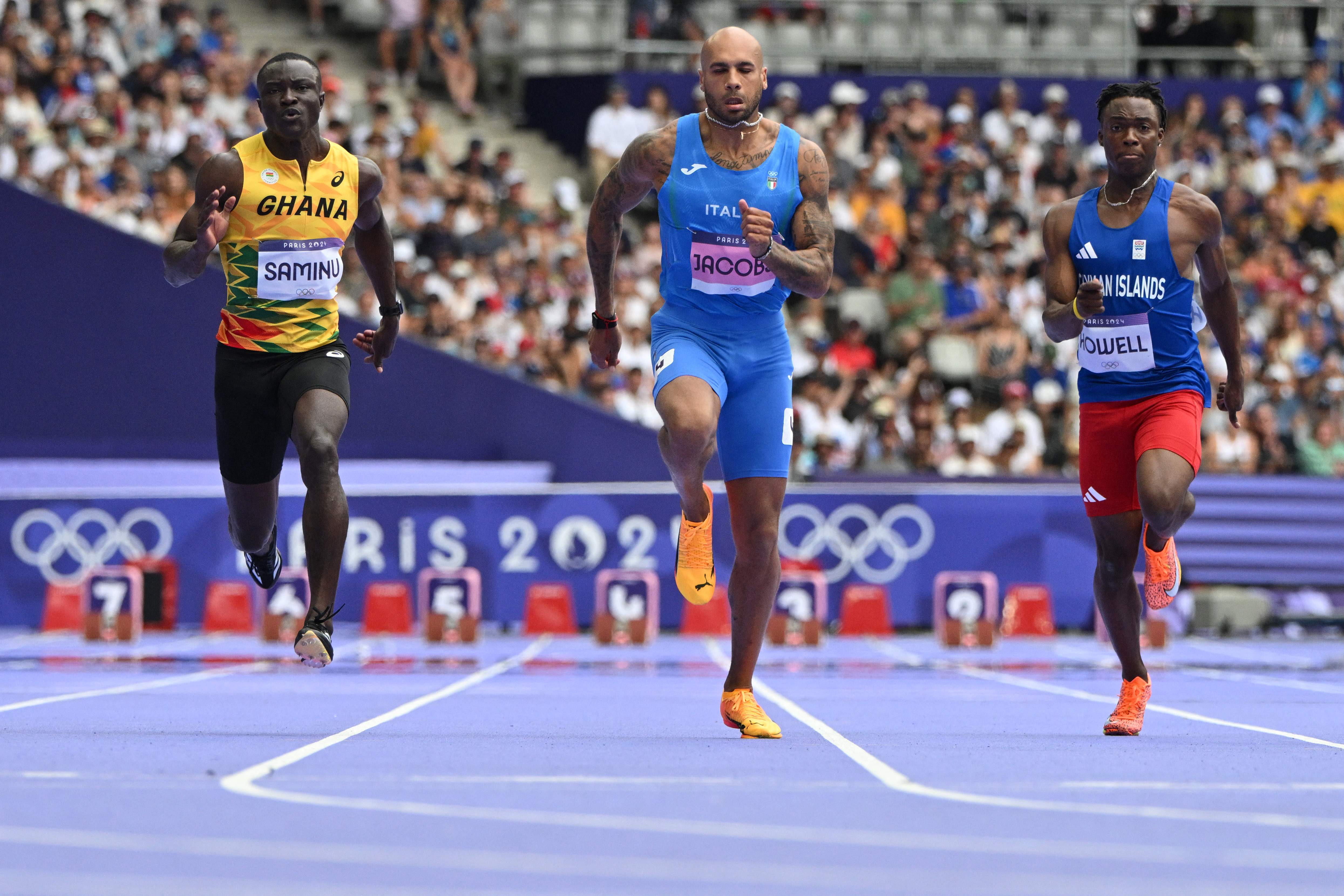 (From L) Ghana's Abdul-Rasheed Saminu, Italy's Lamont Marcell Jacobs and Cayman Islands' Davonte Howell compete in the men's 100m heat of the athletics event at the Paris 2024 Olympic Games at Stade de France in Saint-Denis, north of Paris, on August 3, 2024. (Photo by Jewel SAMAD / AFP)
